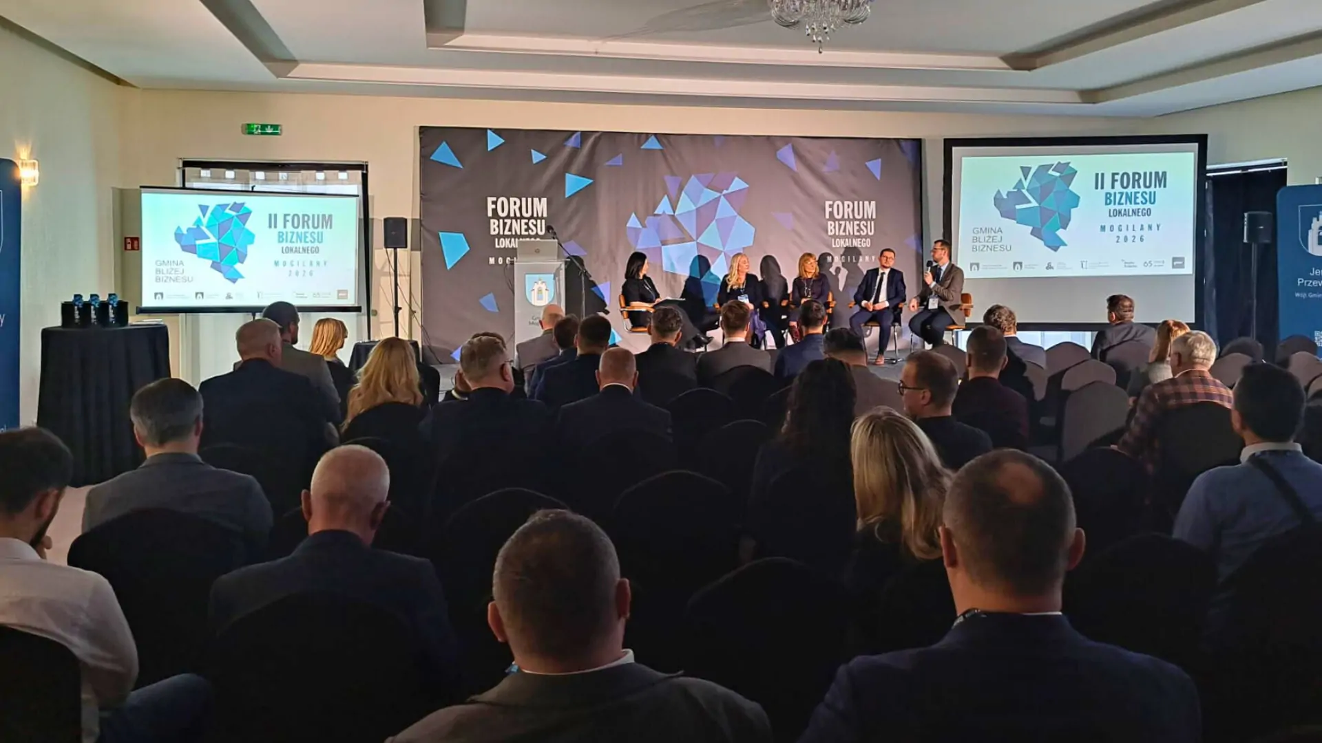 Fotografia przedstawiająca publiczność oglądającą dyskusję ekspertów na scenie. W tle napis: II Forum Biznesu Lokalnego